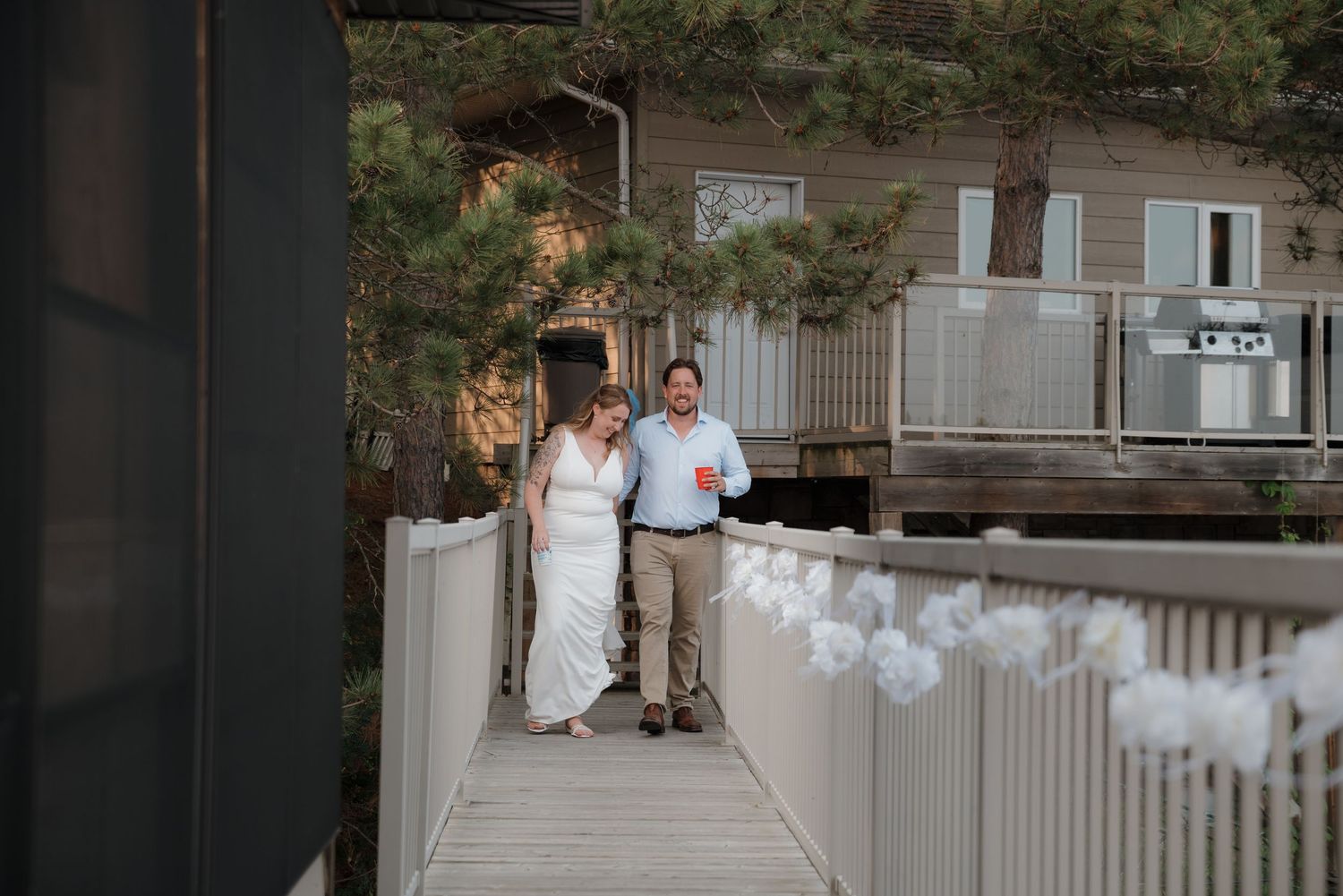 Wedding party stands on a white wooden porch of a historic building during an outdoor celebration.