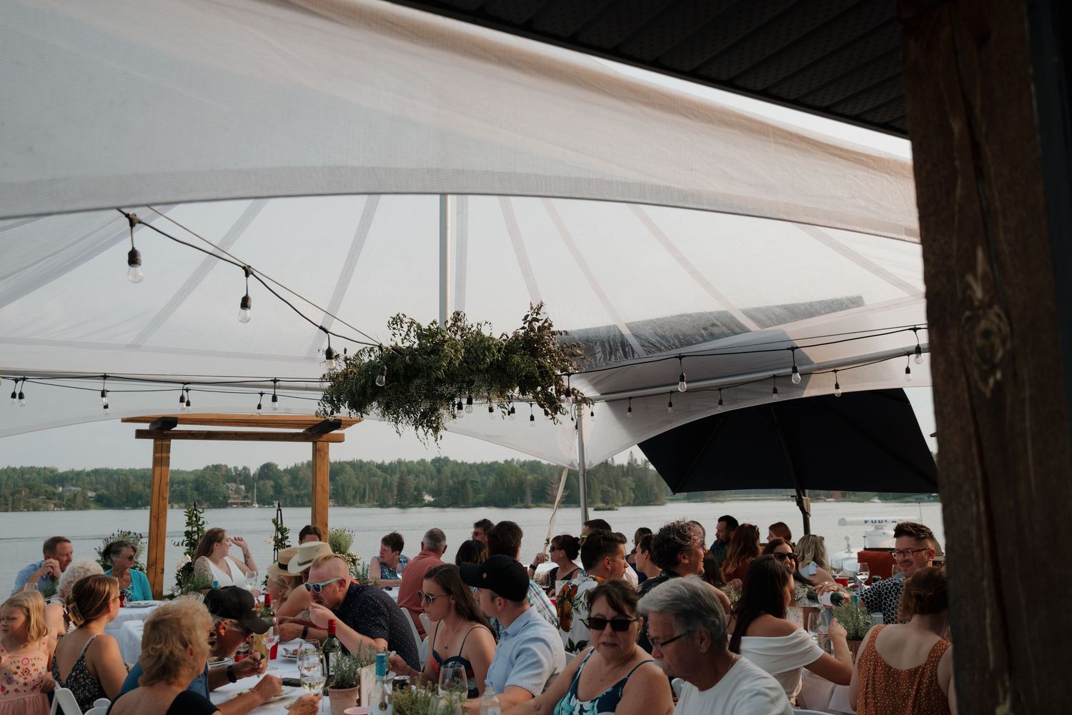 A wedding reception setup under a white tent with string lights and guests mingling in the background.