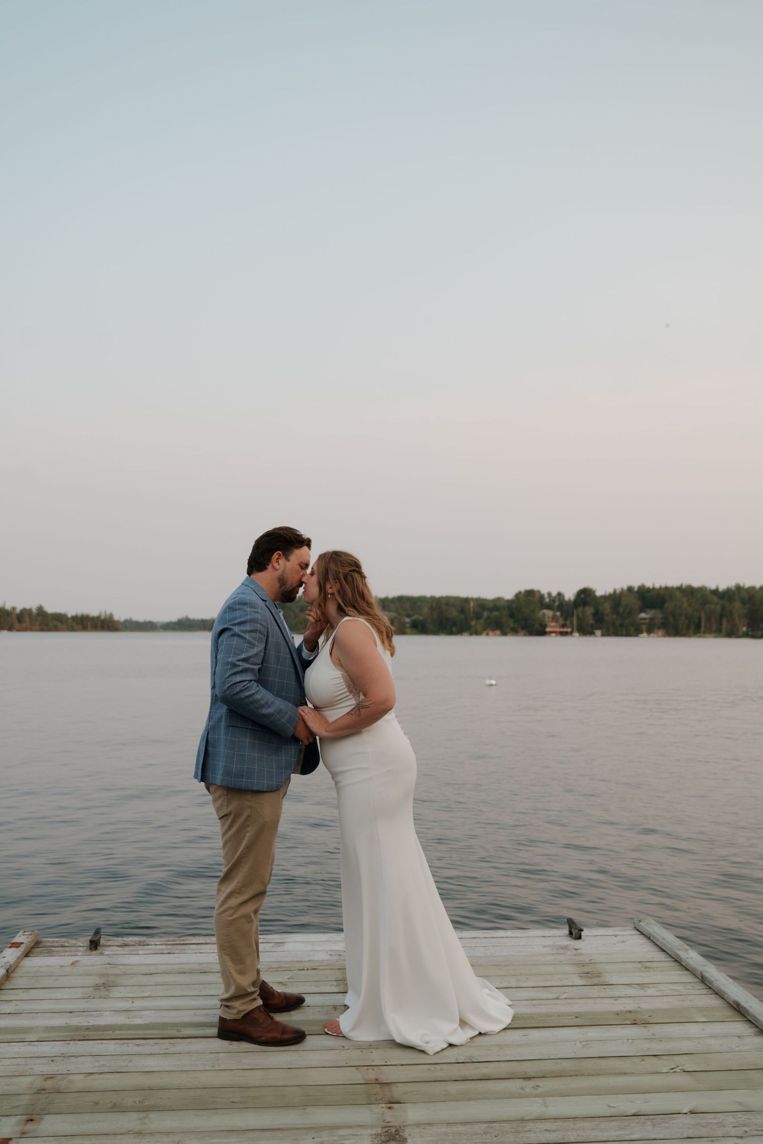 Couple sharing a romantic moment on a wooden dock overlooking a serene lake at sunset.