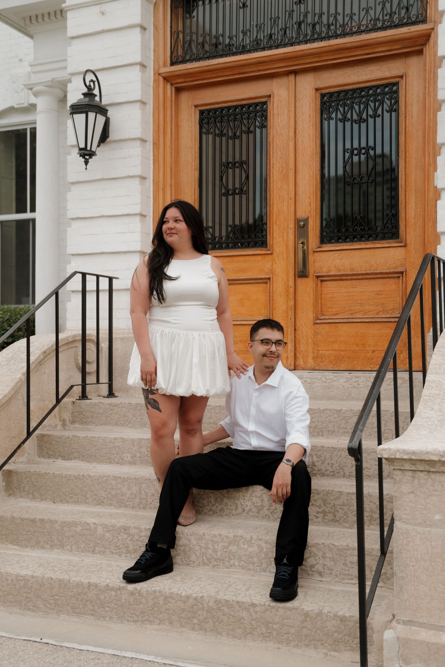 A couple poses on stone steps in front of a grand wooden door with decorative ironwork and a vintage lantern.
