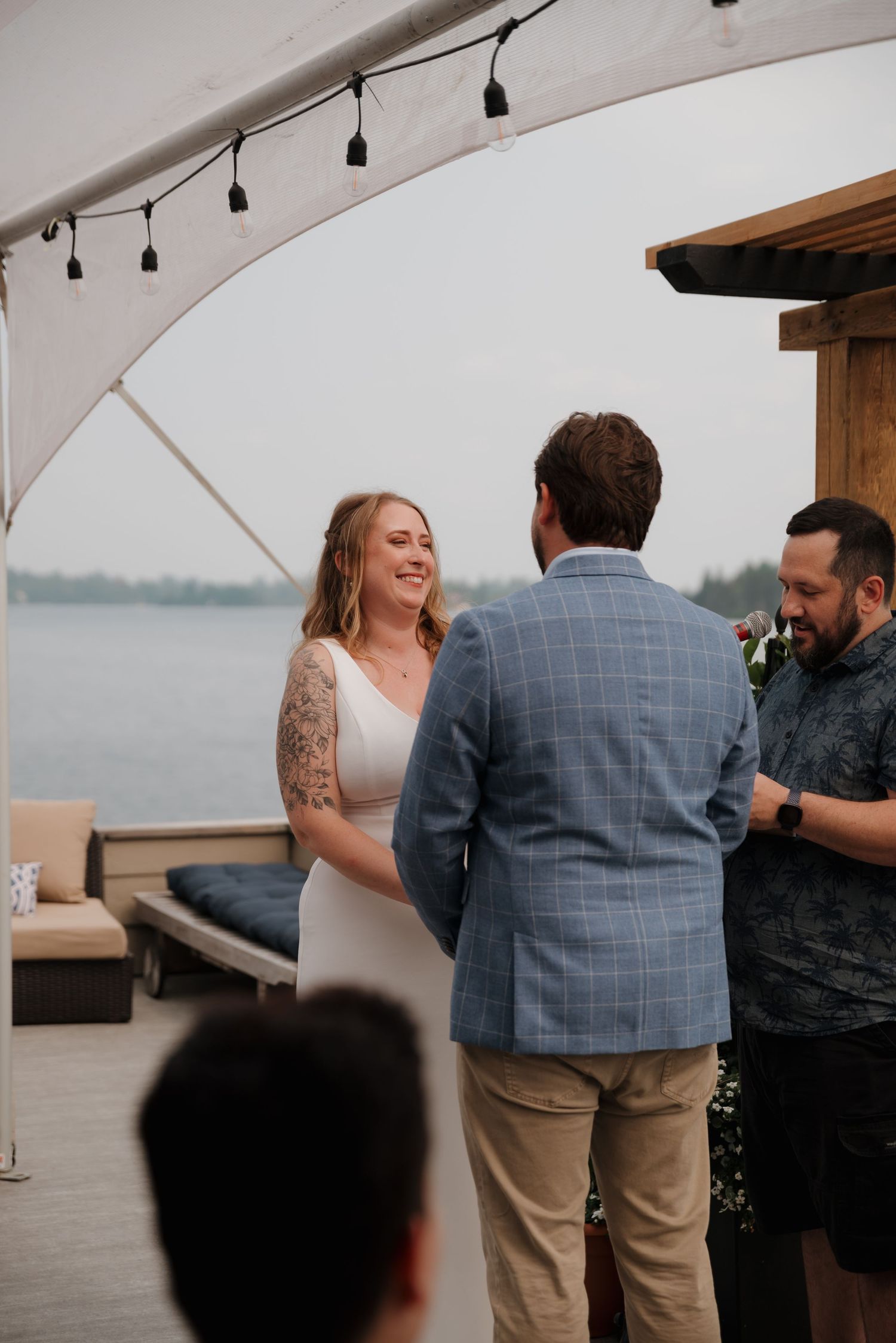 Wedding guests gather under a white canopy tent during an outdoor waterfront celebration.
