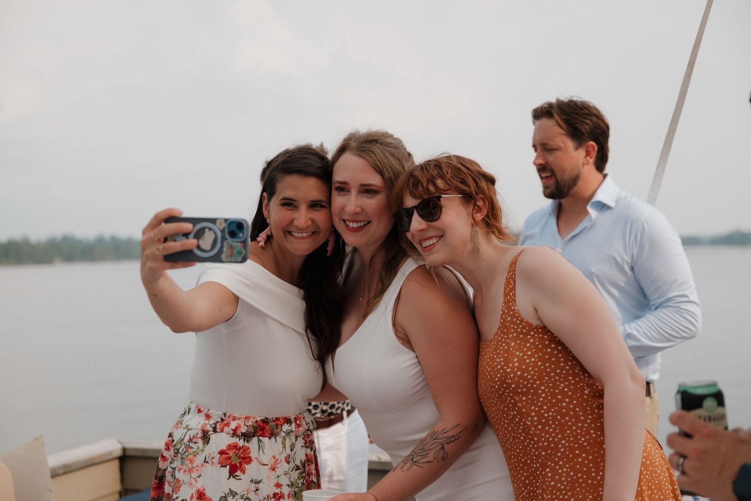 Wedding guests gather on a lakeside deck for celebratory photos at sunset.
