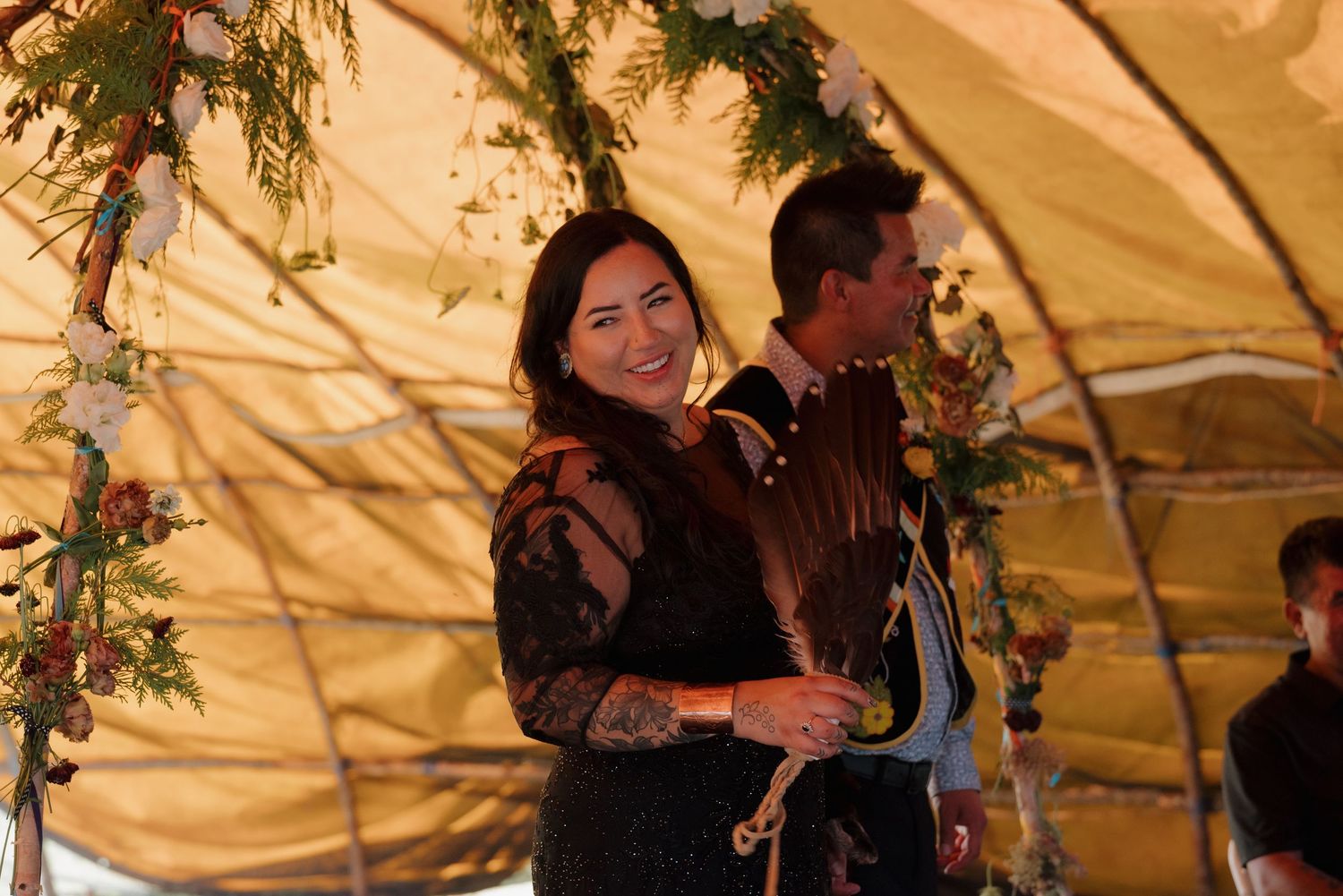 Woman smiling under floral decorated tent canopy at outdoor wedding ceremony.