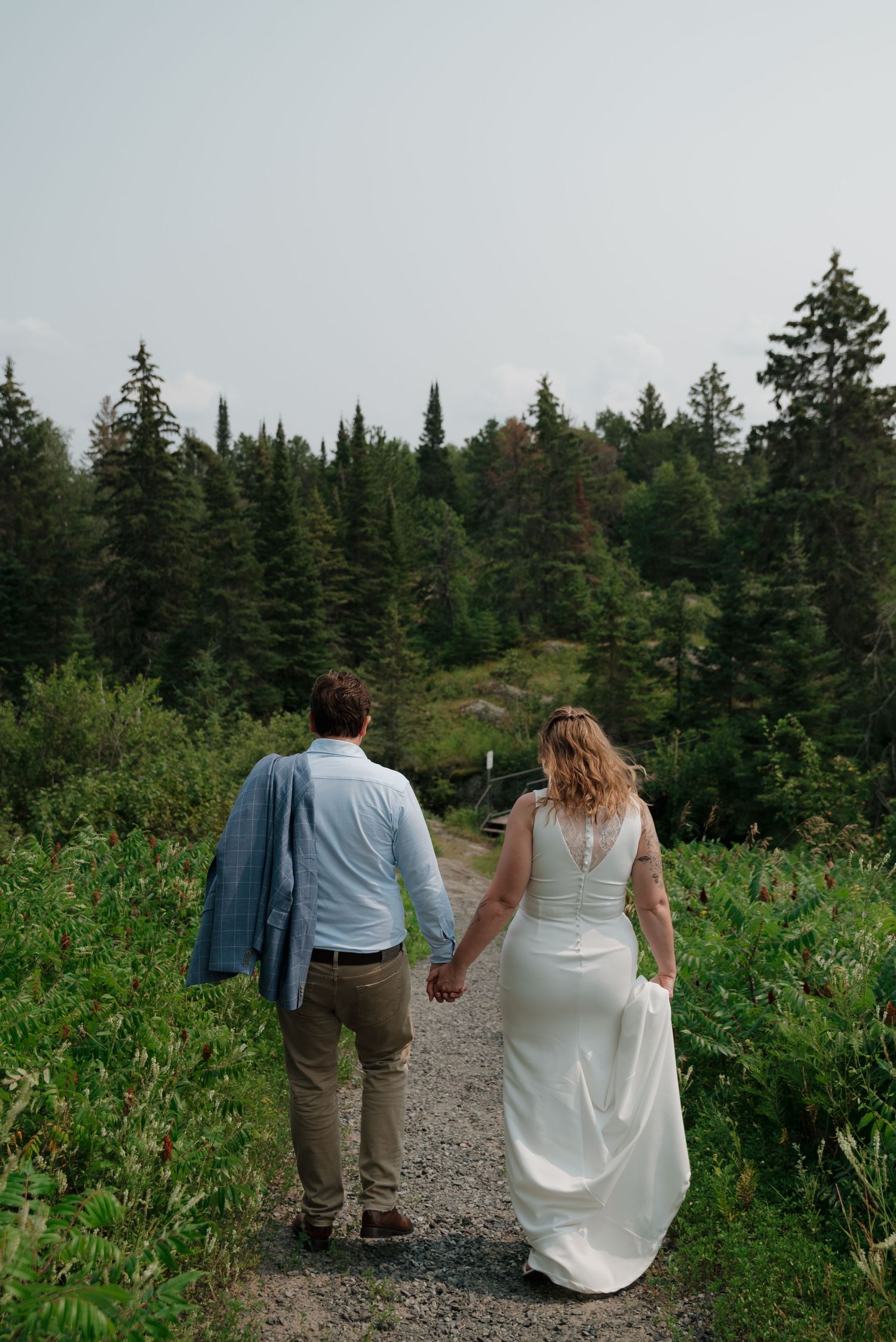 A group walks along a scenic trail surrounded by evergreen trees and lush vegetation.