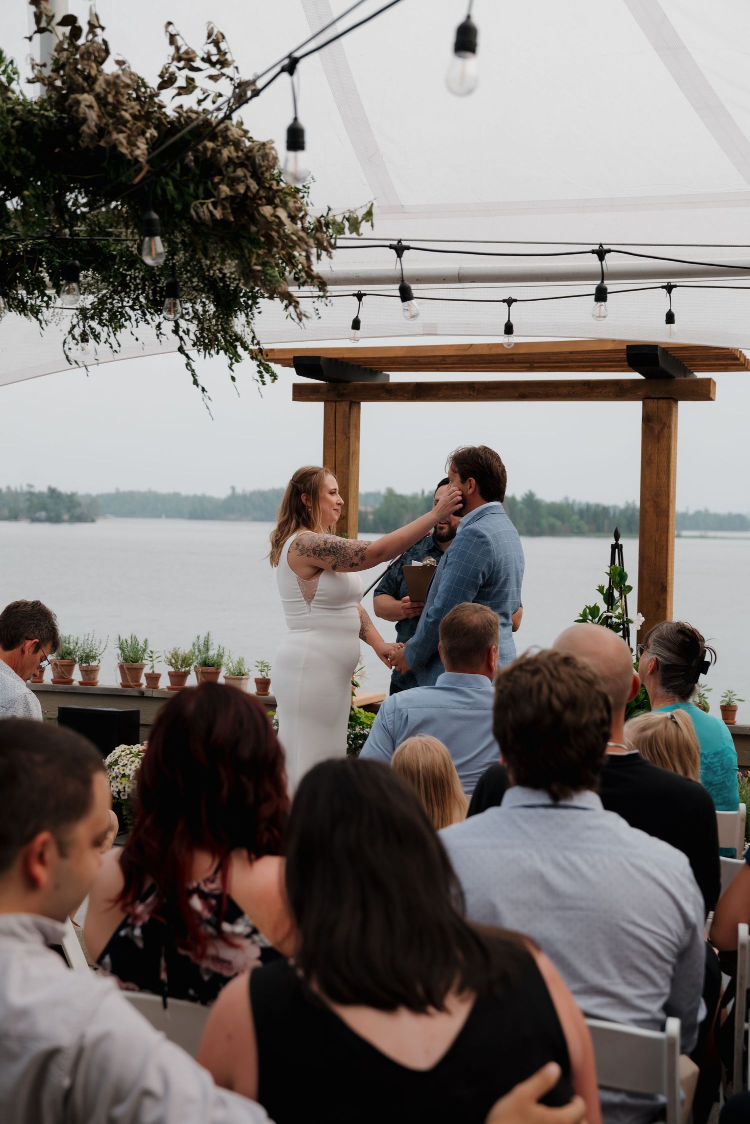 Guests gather under a covered outdoor venue watching a celebration by the waterfront.