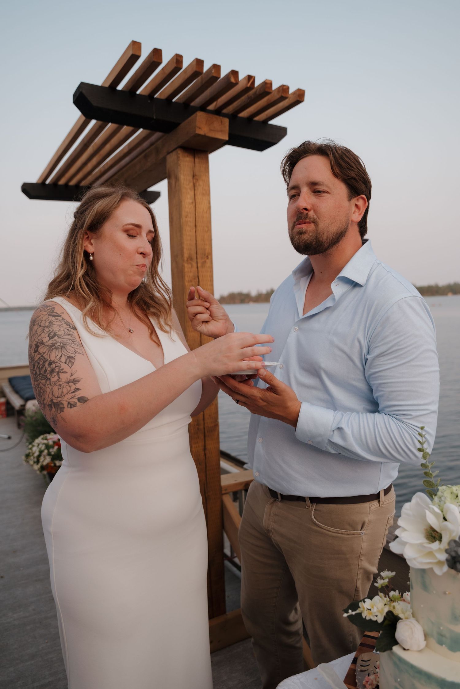 A couple exchanges rings during an intimate waterfront wedding ceremony under a wooden pergola.