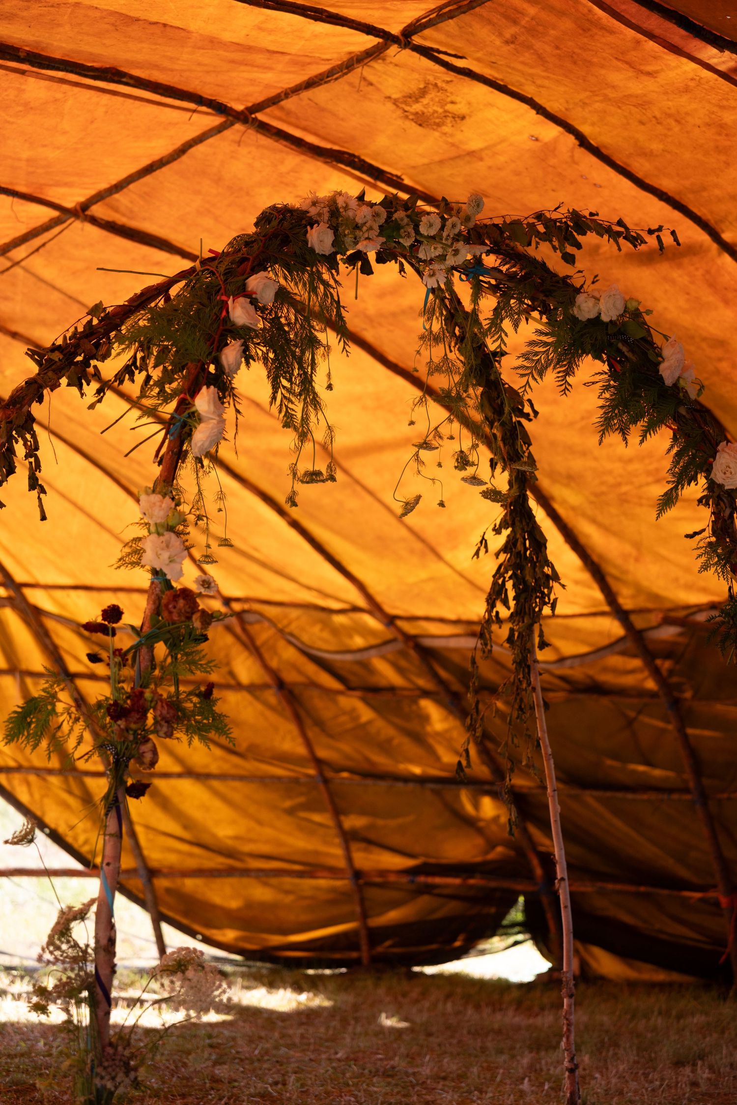 Rustic wooden arch adorned with flowers and greenery inside a warm orange canvas tipi tent.