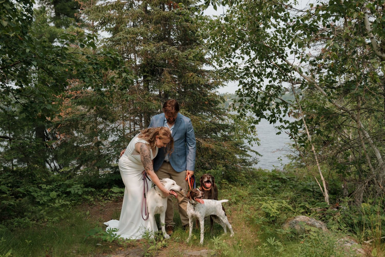 A couple and their dog share a tender moment in a wooded mountain setting with natural greenery.