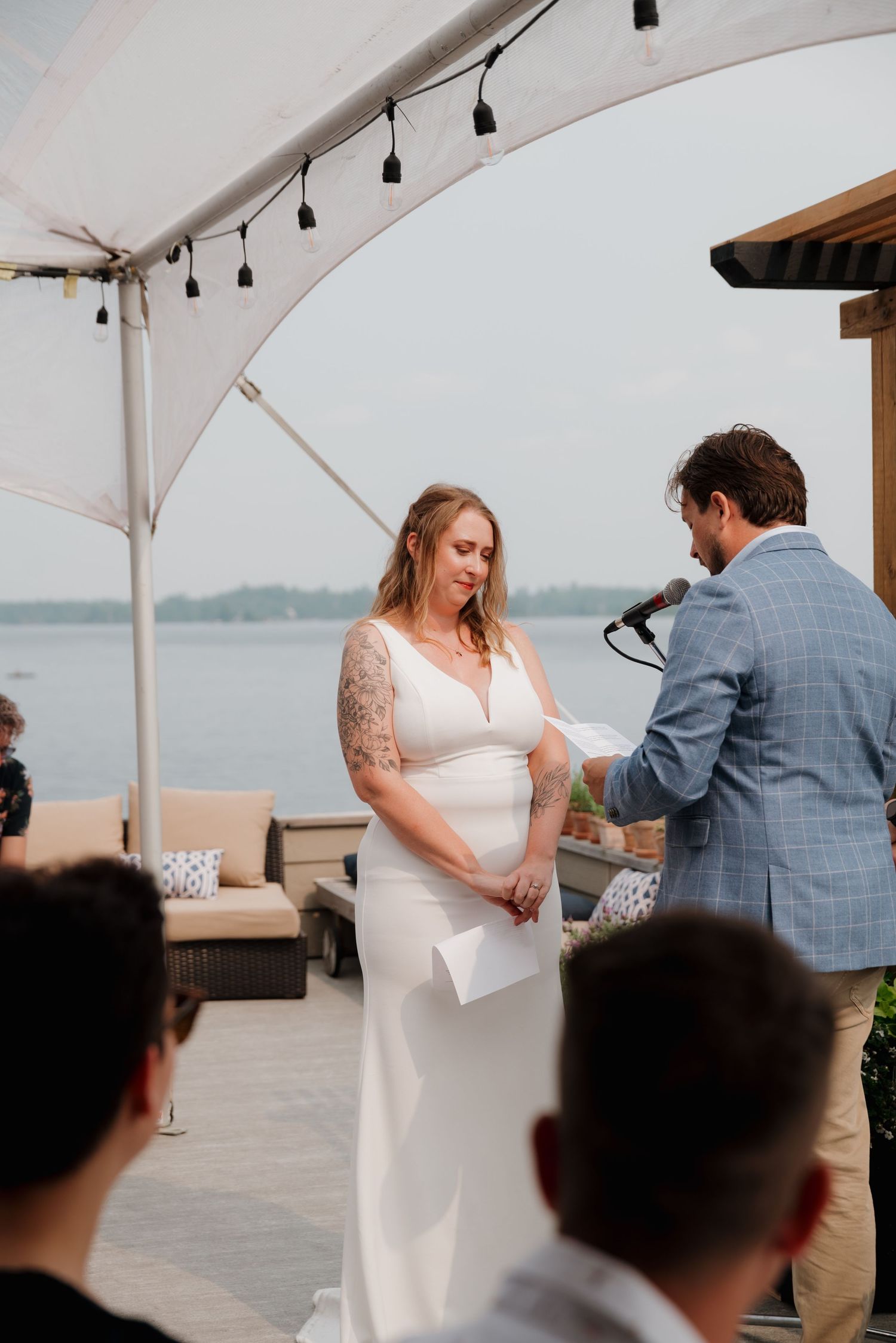 A couple shares a special moment during their wedding ceremony under a white tent by the water.