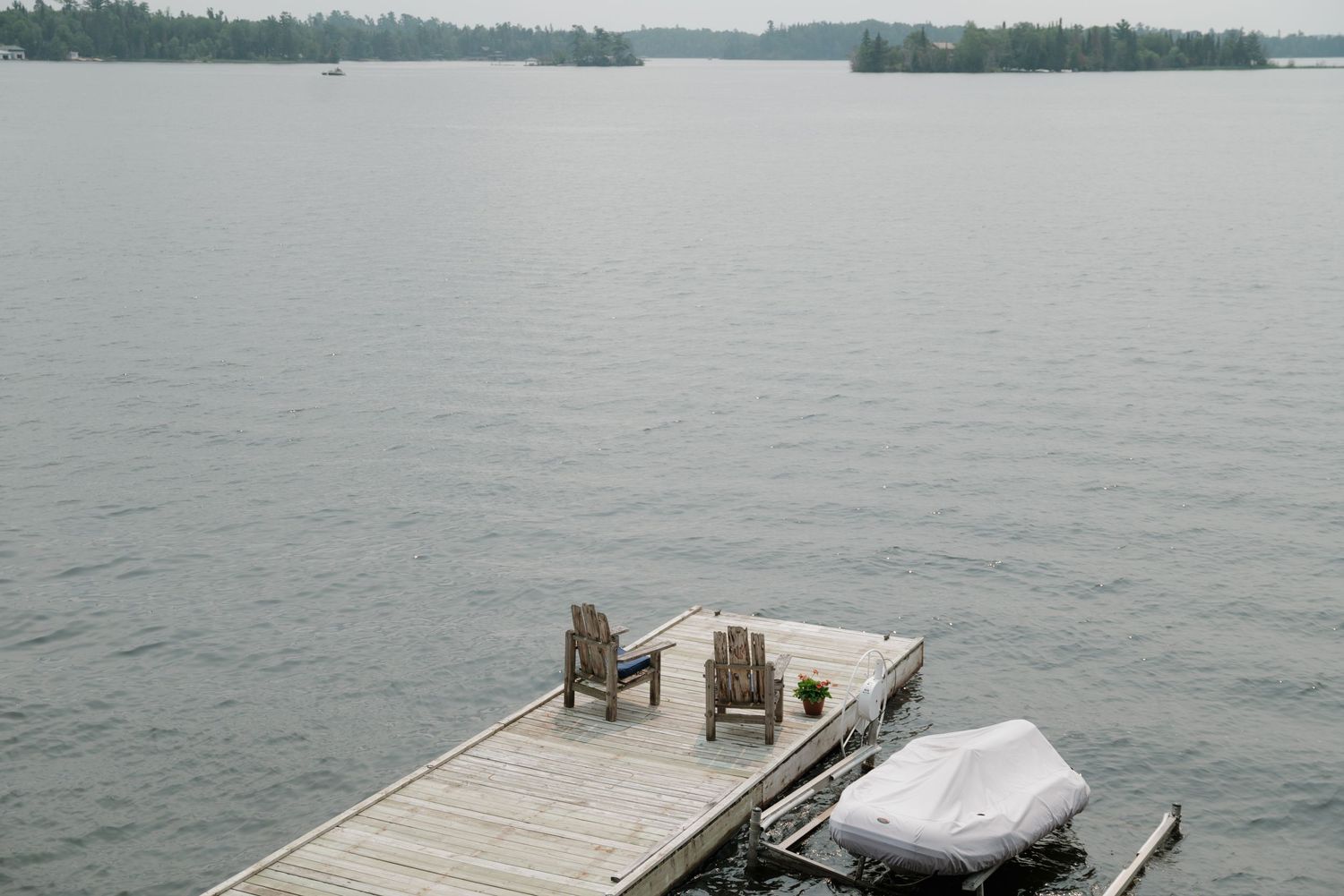 Peaceful lakefront view with wooden dock and distant tree-lined shore.