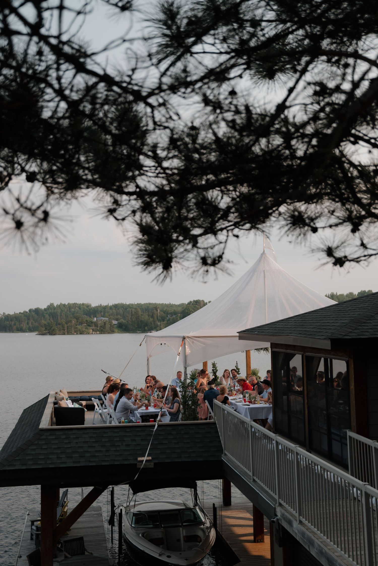 A waterfront wedding venue with white tent and dock overlooking a scenic lake at dusk.