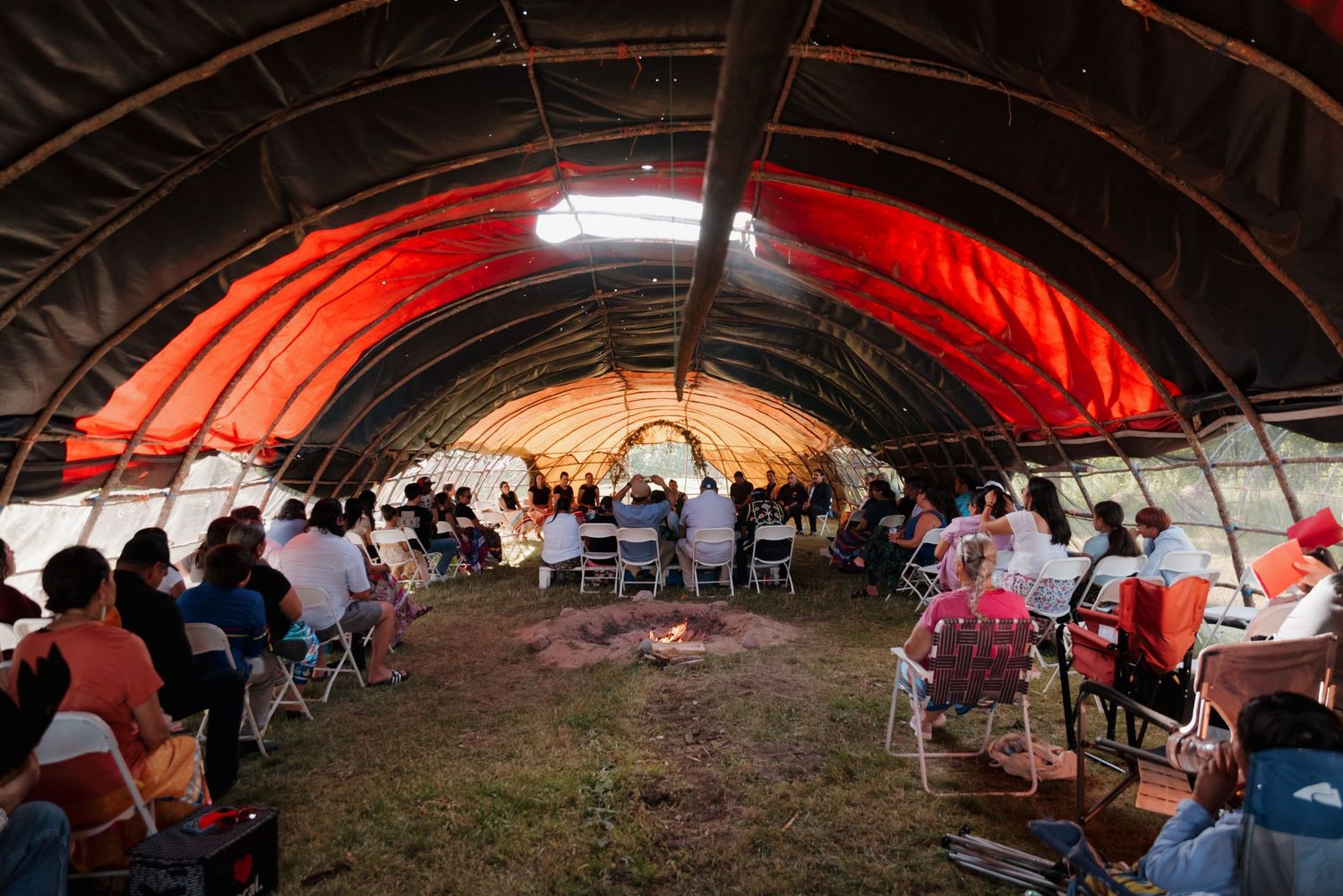 Wide interior view of traditional Native American ceremonial dome structure filled with seated wedding guests around central fire.