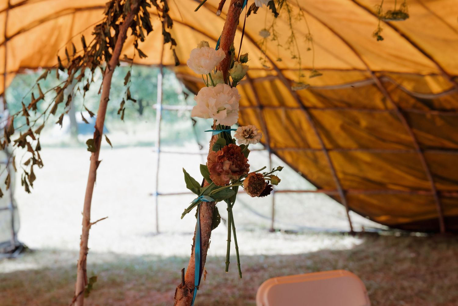 Rustic wedding tent decorated with hanging floral arrangements featuring white blooms and greenery under a golden canopy.