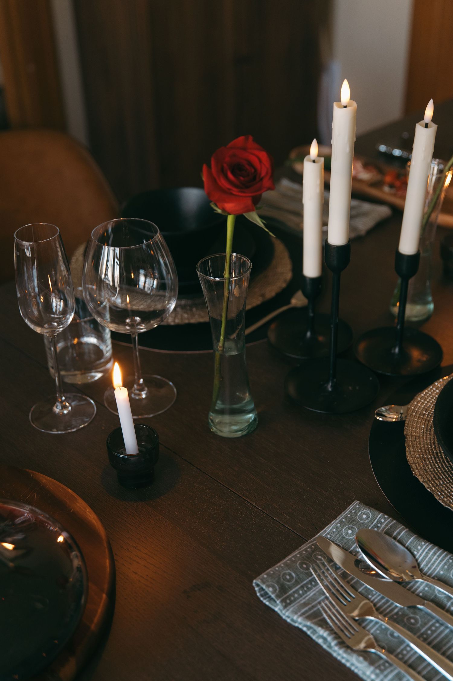 Romantic candlelit dinner table with red rose, wine glasses, and candles.