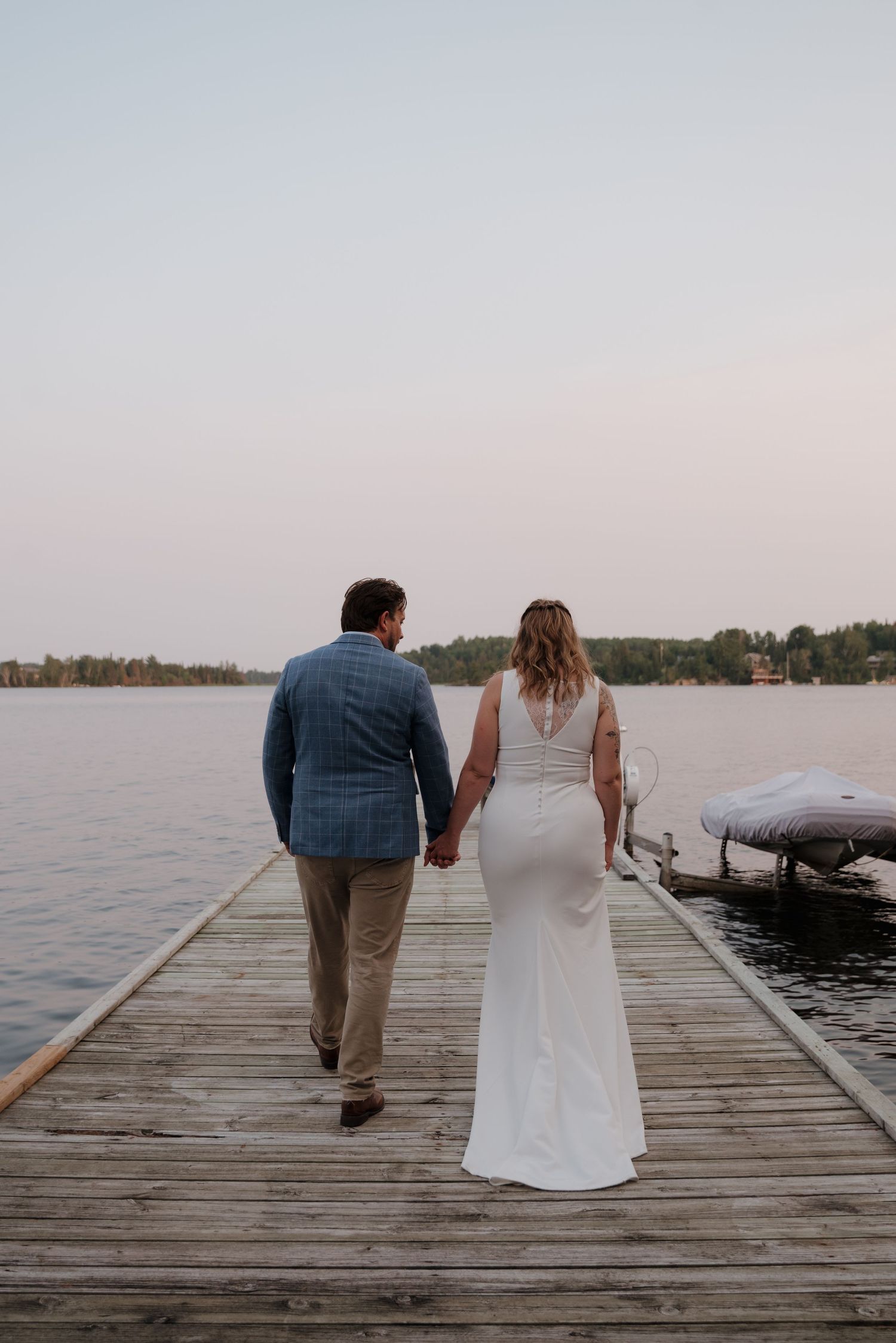 Couple walking together on a wooden dock by the lake at sunset.