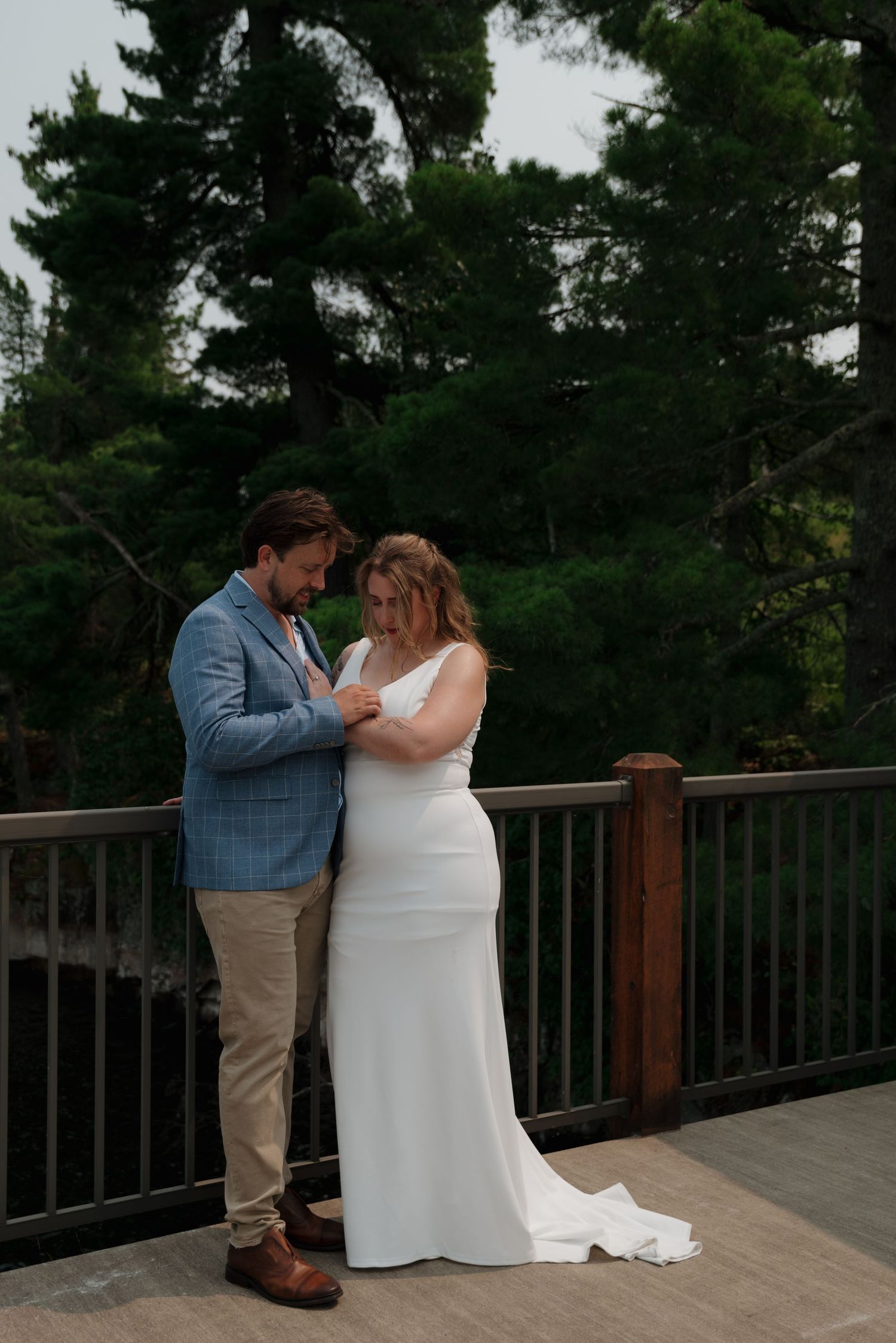 A couple embracing on a wooden deck overlooking a scenic lake and forest.
