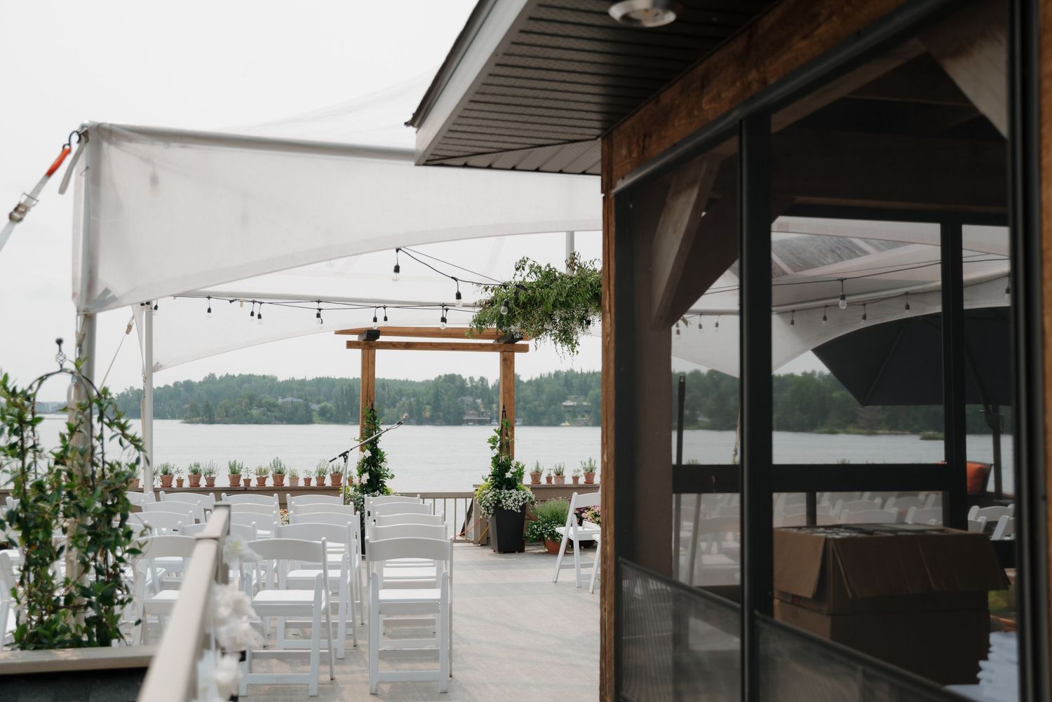 Covered outdoor wedding venue with white chairs set up overlooking a serene lake.