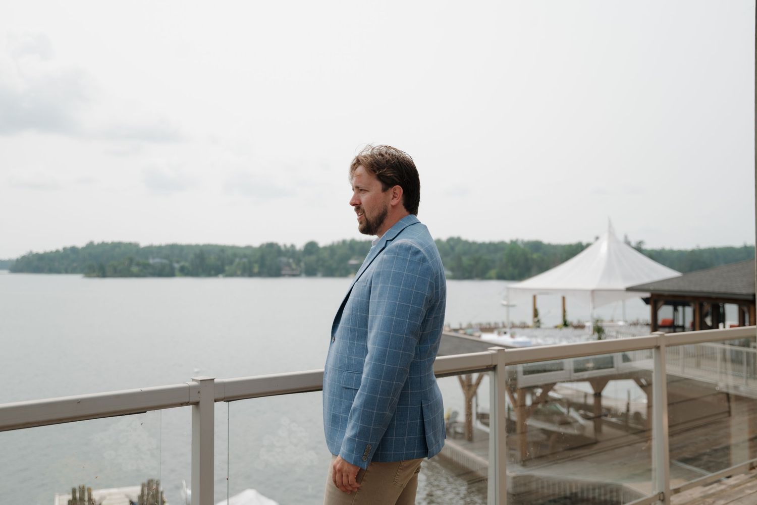 Person in blue blazer looking out over lake from deck during event.