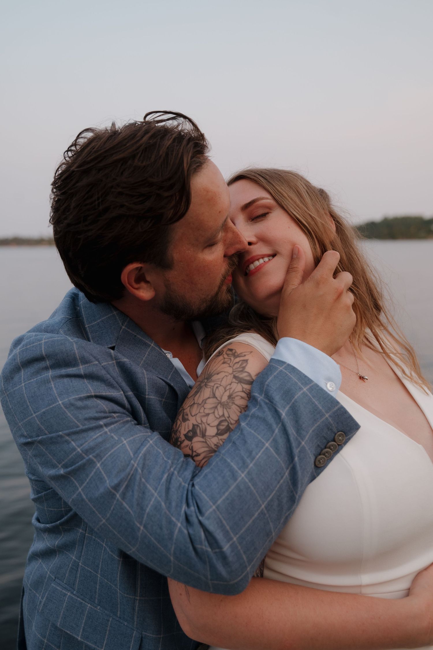 A romantic moment shared between a couple on a lakeside dock at sunset.