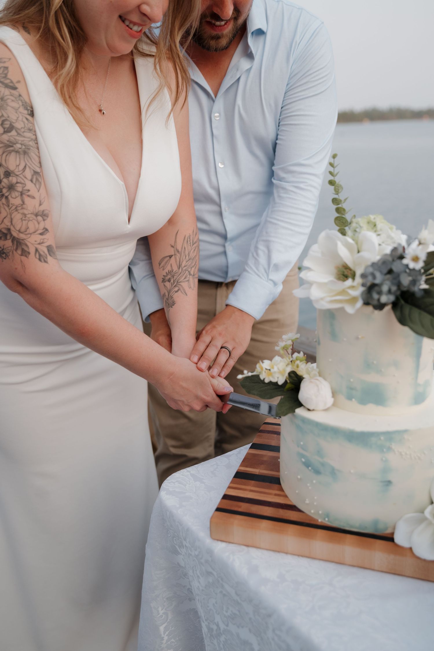 A couple cutting into their elegant blue and white wedding cake together on a wooden table.