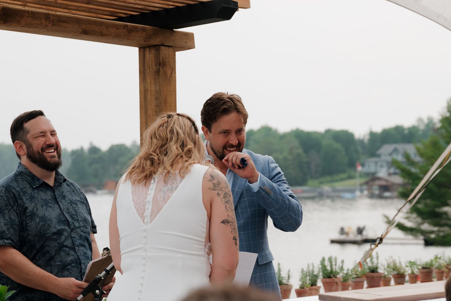 Wedding ceremony setup under a wooden pergola with white floral arrangements by the waterfront.