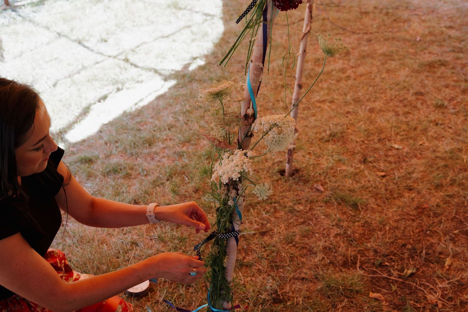 Woman arranging wildflowers on a decorative outdoor floral installation at a garden event.