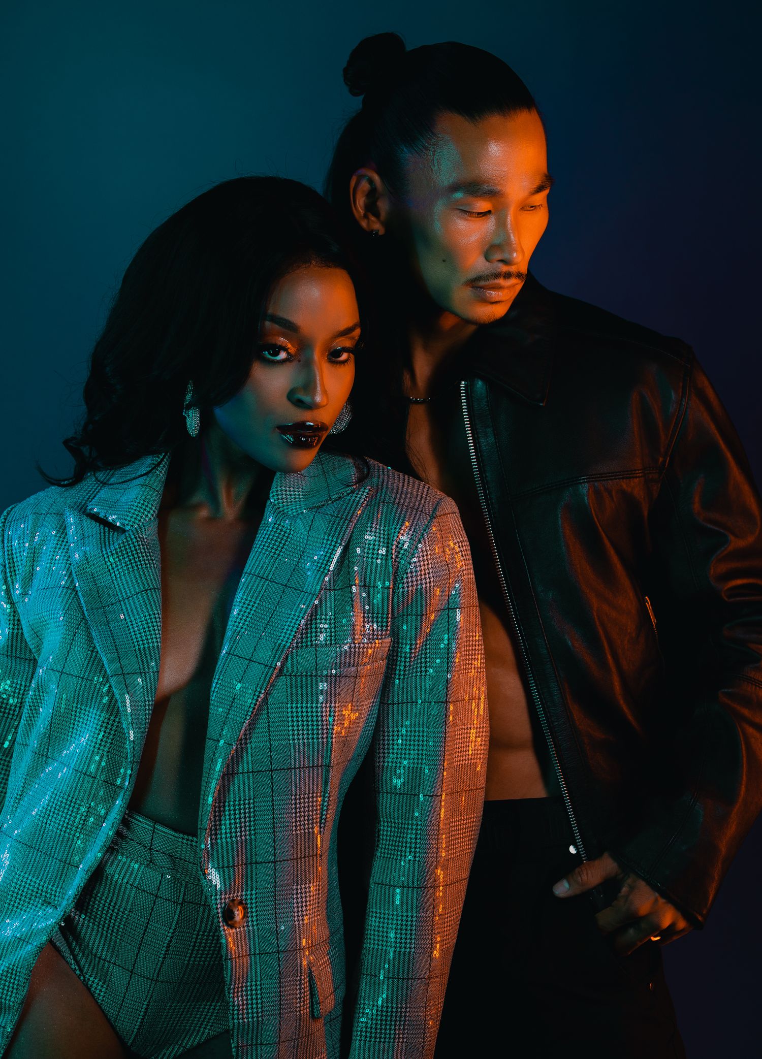 Stylish couple posing in dramatic neon lighting, woman in sequin jacket, man in leather jacket.