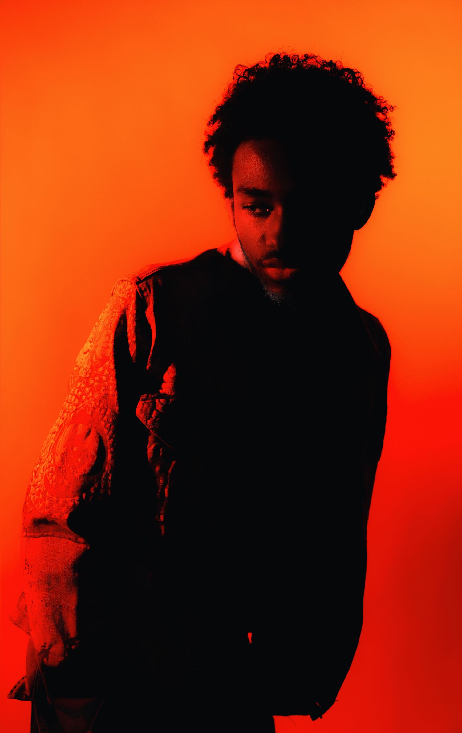 Young person with curly hair poses dramatically against a vivid red-orange background in dark clothing.