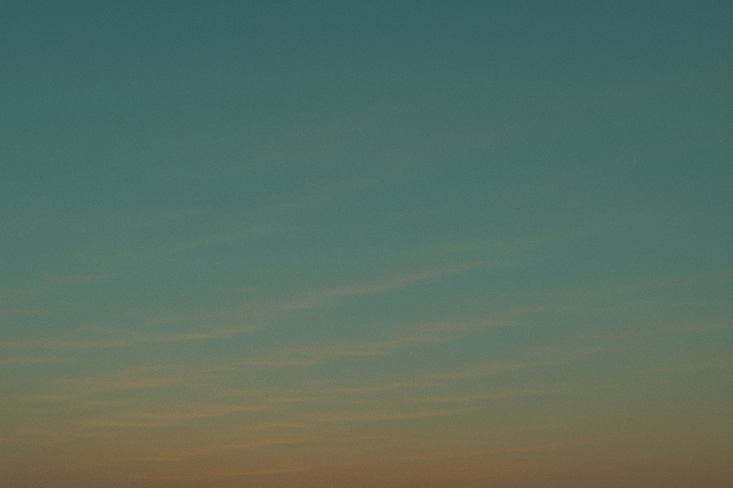 A serene twilight sky with soft teal and warm orange gradient hues and wispy clouds near the horizon.