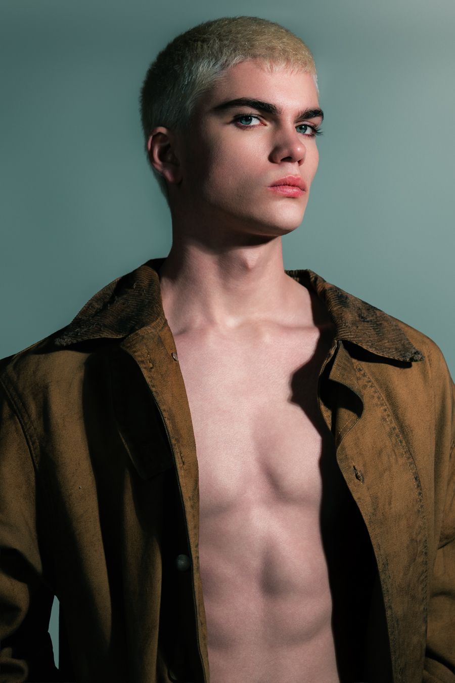 Young man with bleached hair wearing an open brown jacket, showcasing a bold editorial fashion look.