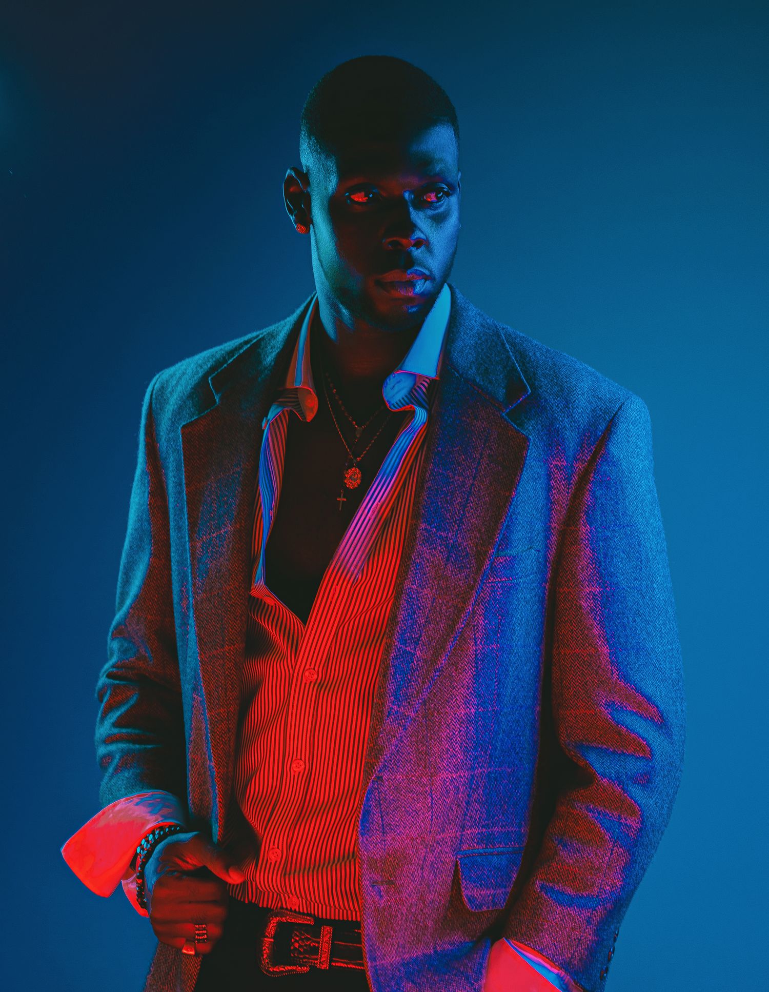 Man in blazer and red shirt posed under dramatic blue and red studio lighting.