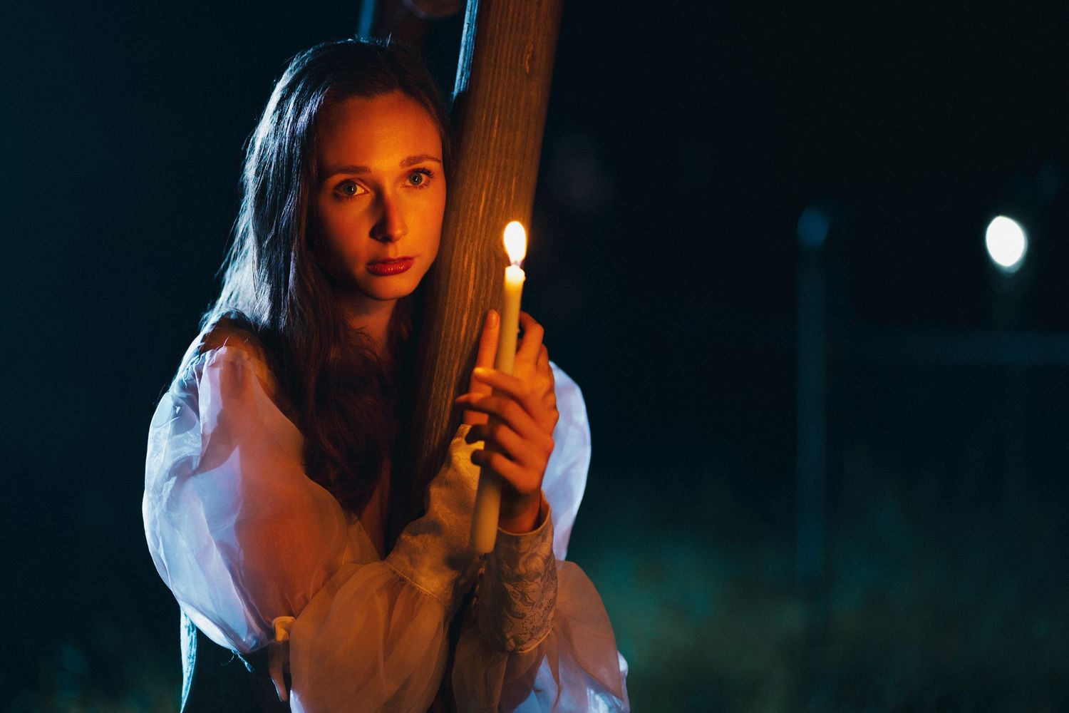 Young woman in white dress holding a lit candle at night, creating a mysterious, gothic atmosphere.