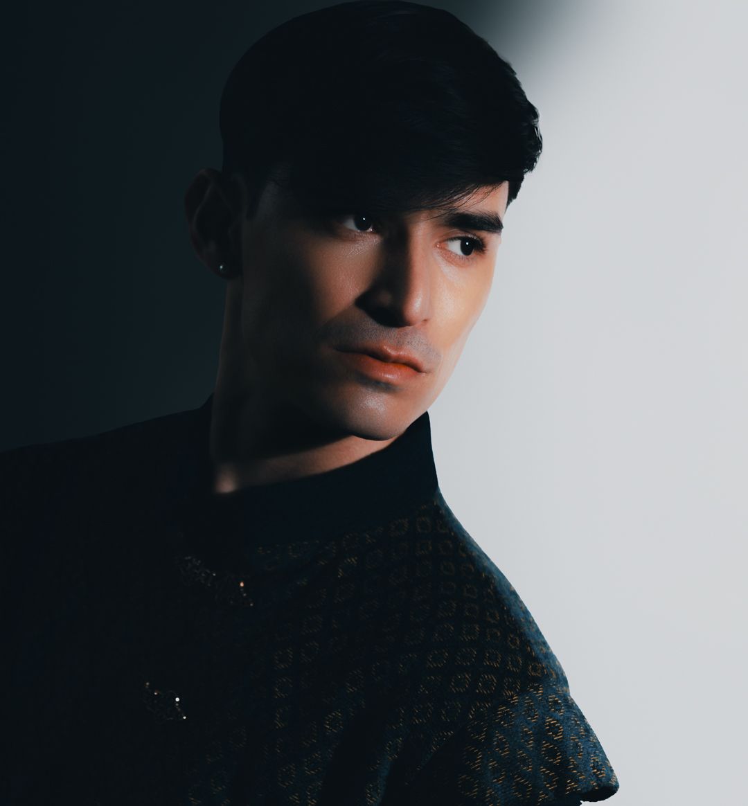 Young man with dark hair wearing a black turtleneck, posing against a light gray background in a moody portrait.