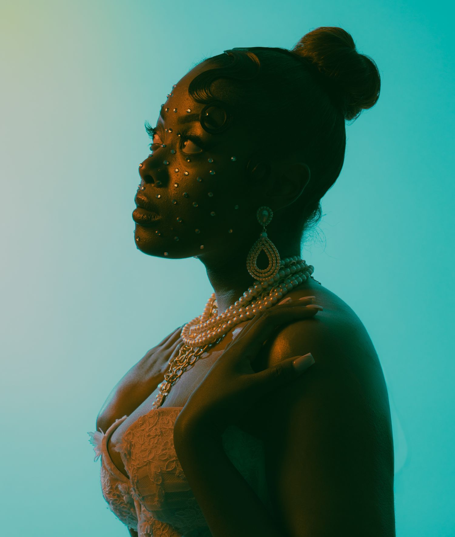 A Black woman in profile with jeweled face gems, pearl necklace, and elegant earrings against a teal gradient background.