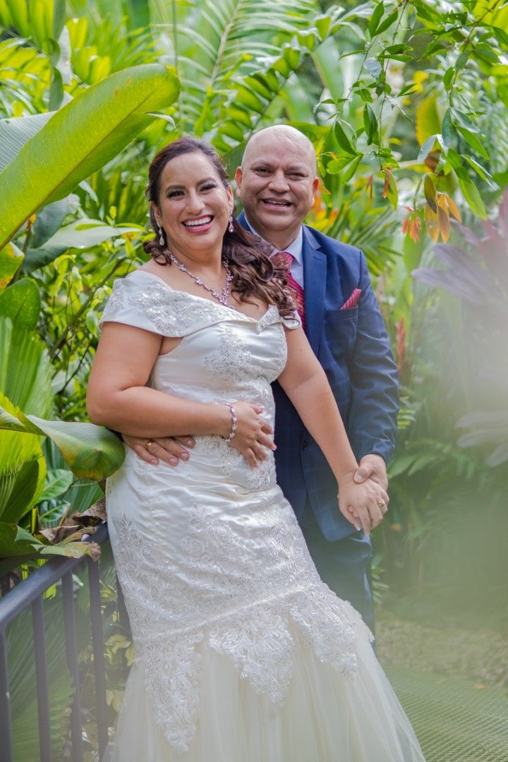 Newlywed couple posing for photos in a lush tropical garden setting wearing wedding attire.