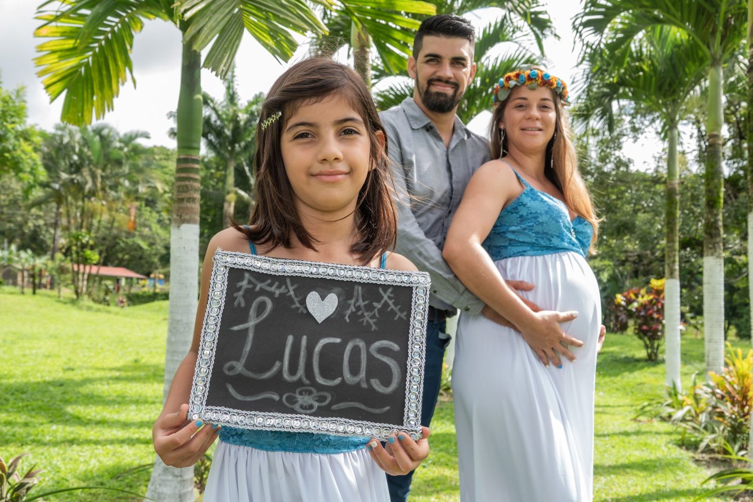 Family poses together as child displays Lucas name sign during maternity photoshoot.