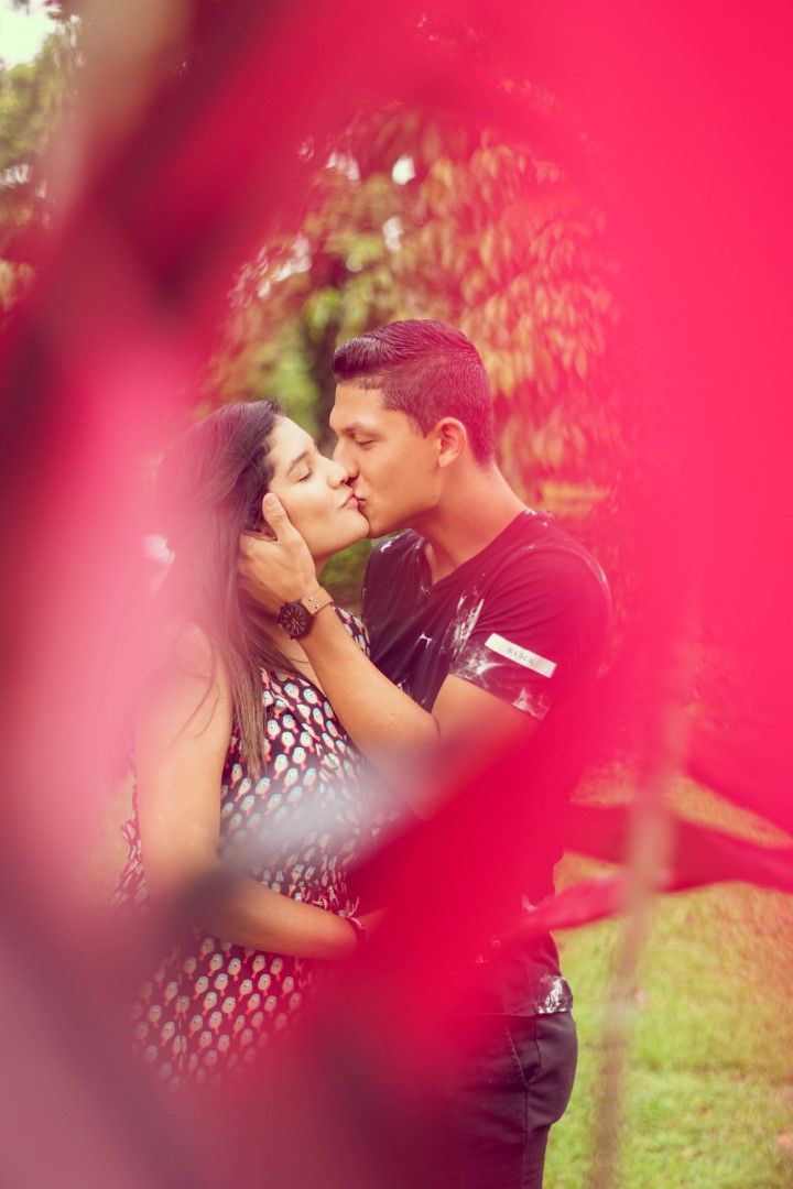 A romantic couple sharing an intimate kiss framed by red flowers in a garden setting.