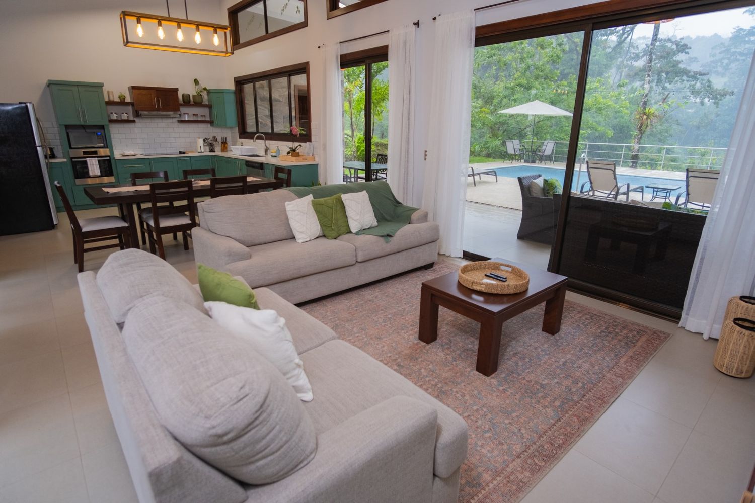 Modern living room interior with beige sofa, wood furniture, and mountain views through large windows.