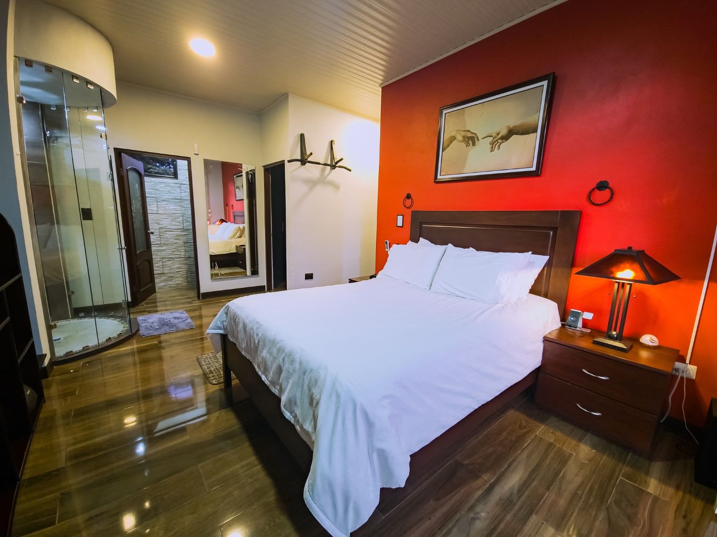 Modern bedroom with red accent wall, dark wood floors, and white bedding.
