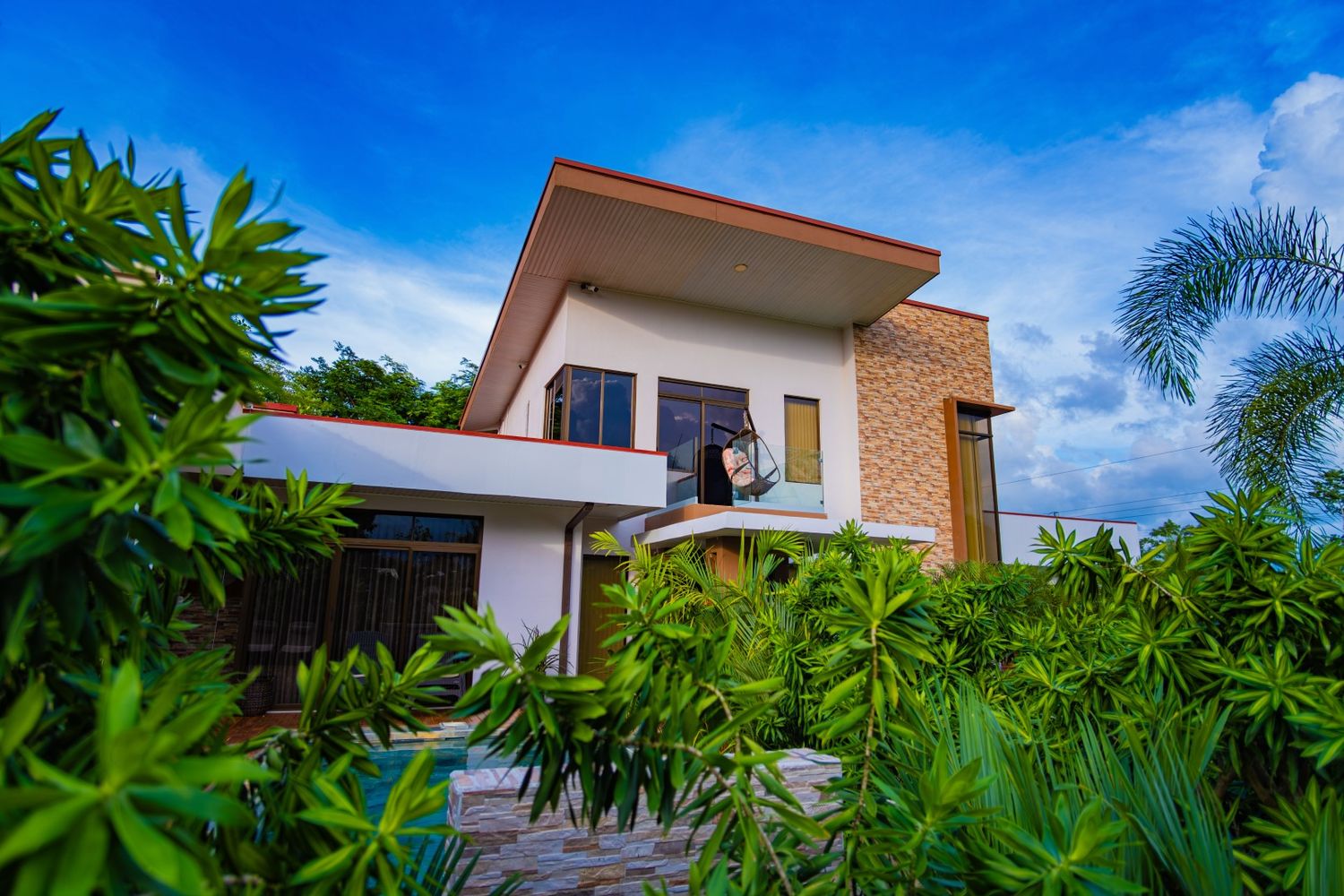 Modern tropical villa with contemporary architecture surrounded by lush greenery against blue sky.