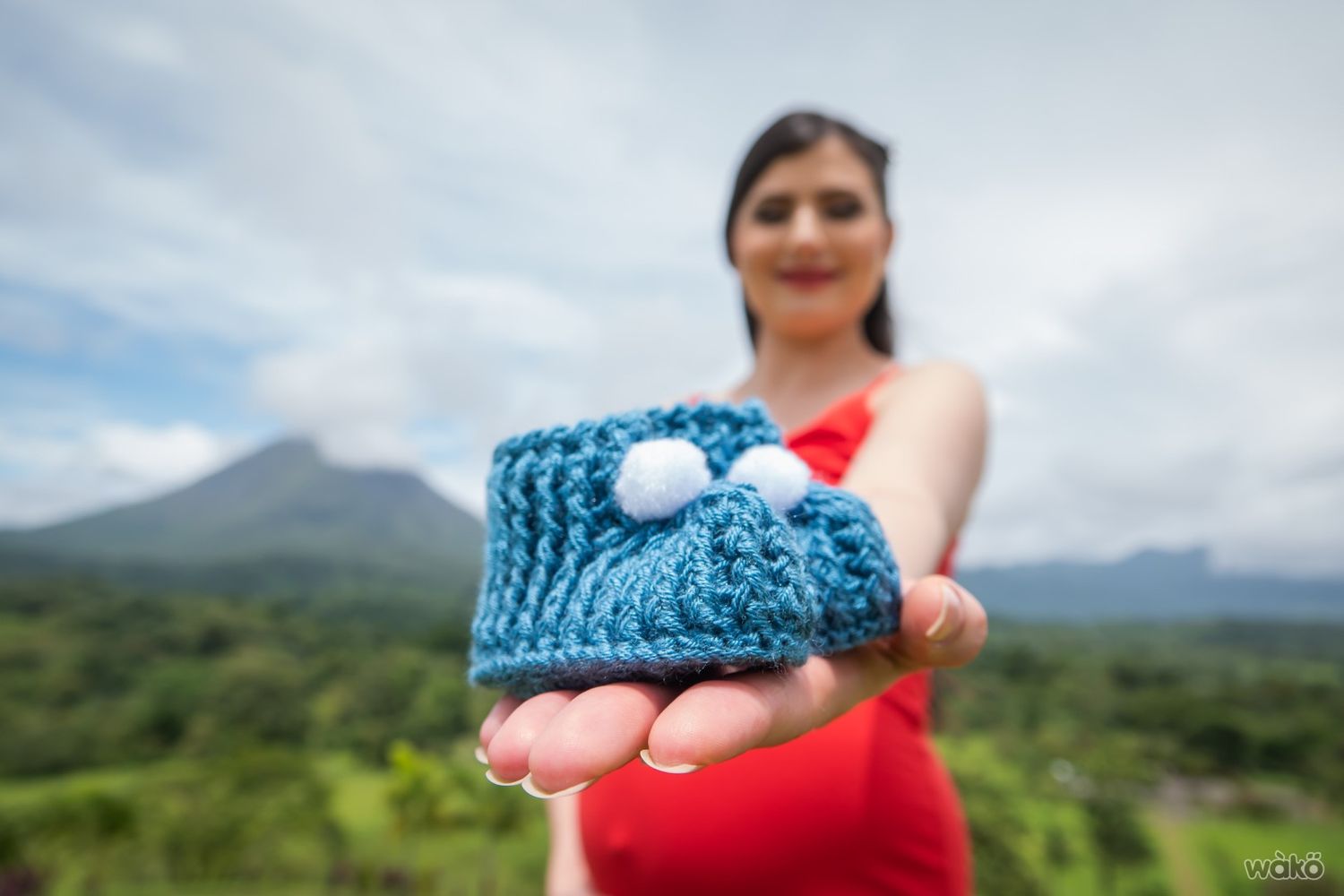 Close up of knitted baby booties held up against mountain scenery background.