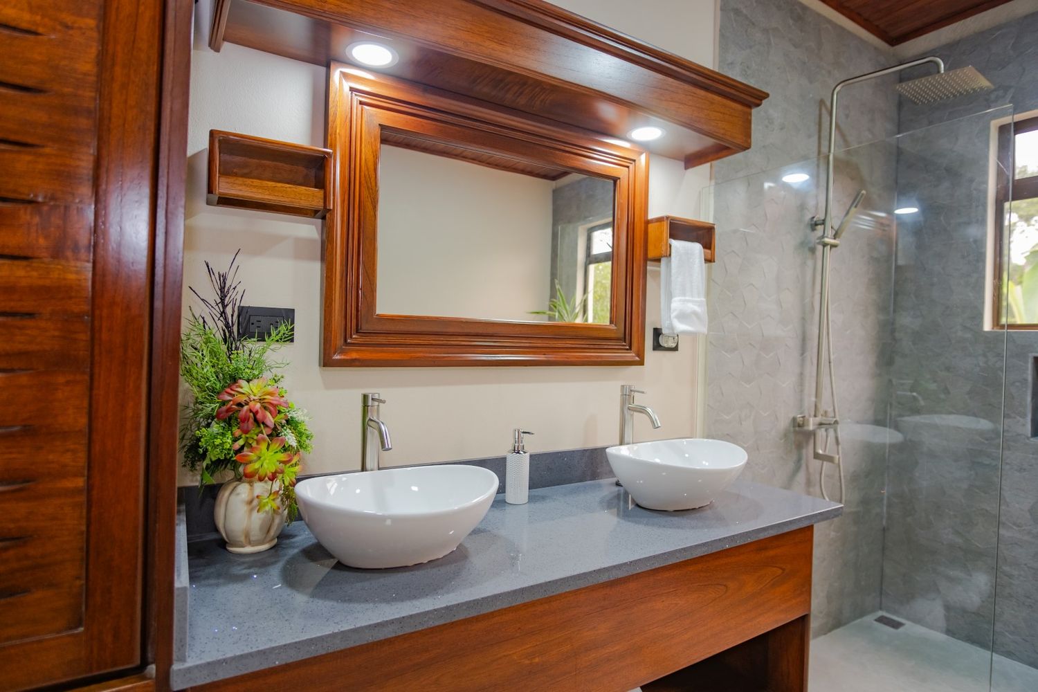 Modern bathroom featuring vessel sink, wooden vanity, and gray tile walls with glass shower enclosure.