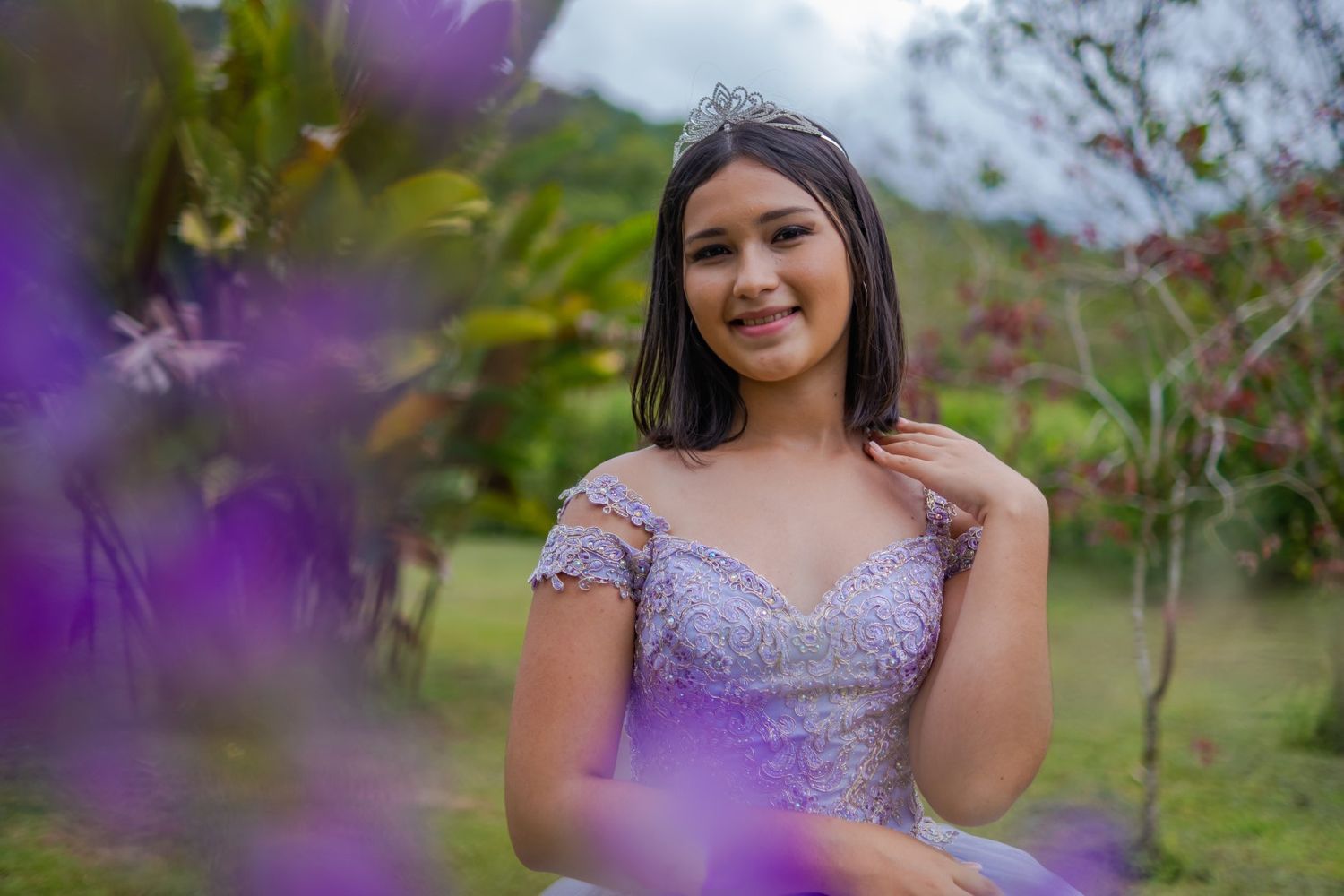 Portrait in purple formal dress framed by soft focus flowers in foreground.