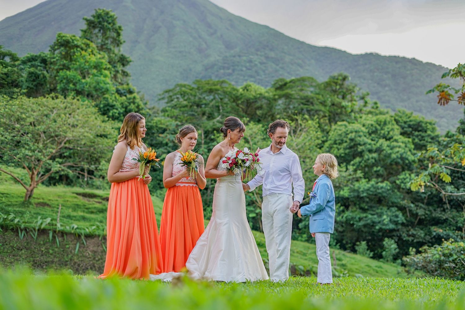 A wedding party poses in a lush tropical garden with a majestic mountain backdrop.