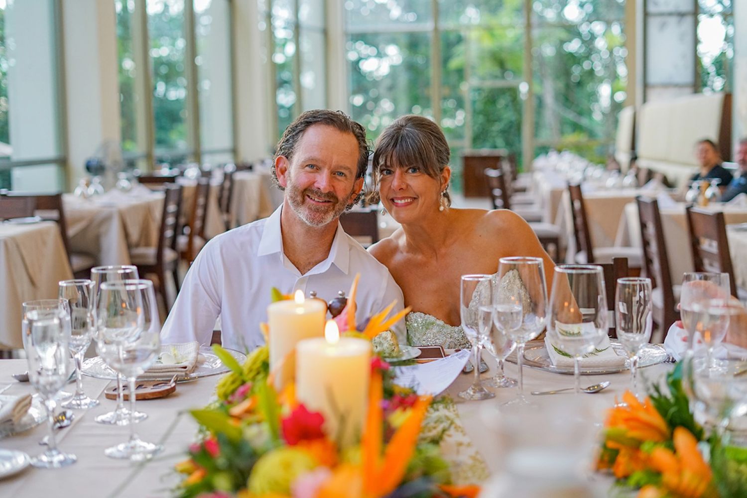 A romantic wedding reception table decorated with elegant glassware and vibrant floral centerpieces with candles.