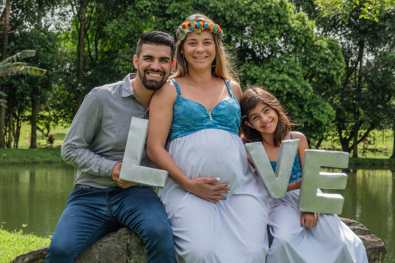 Maternity photoshoot in park setting with family posing together by a pond.