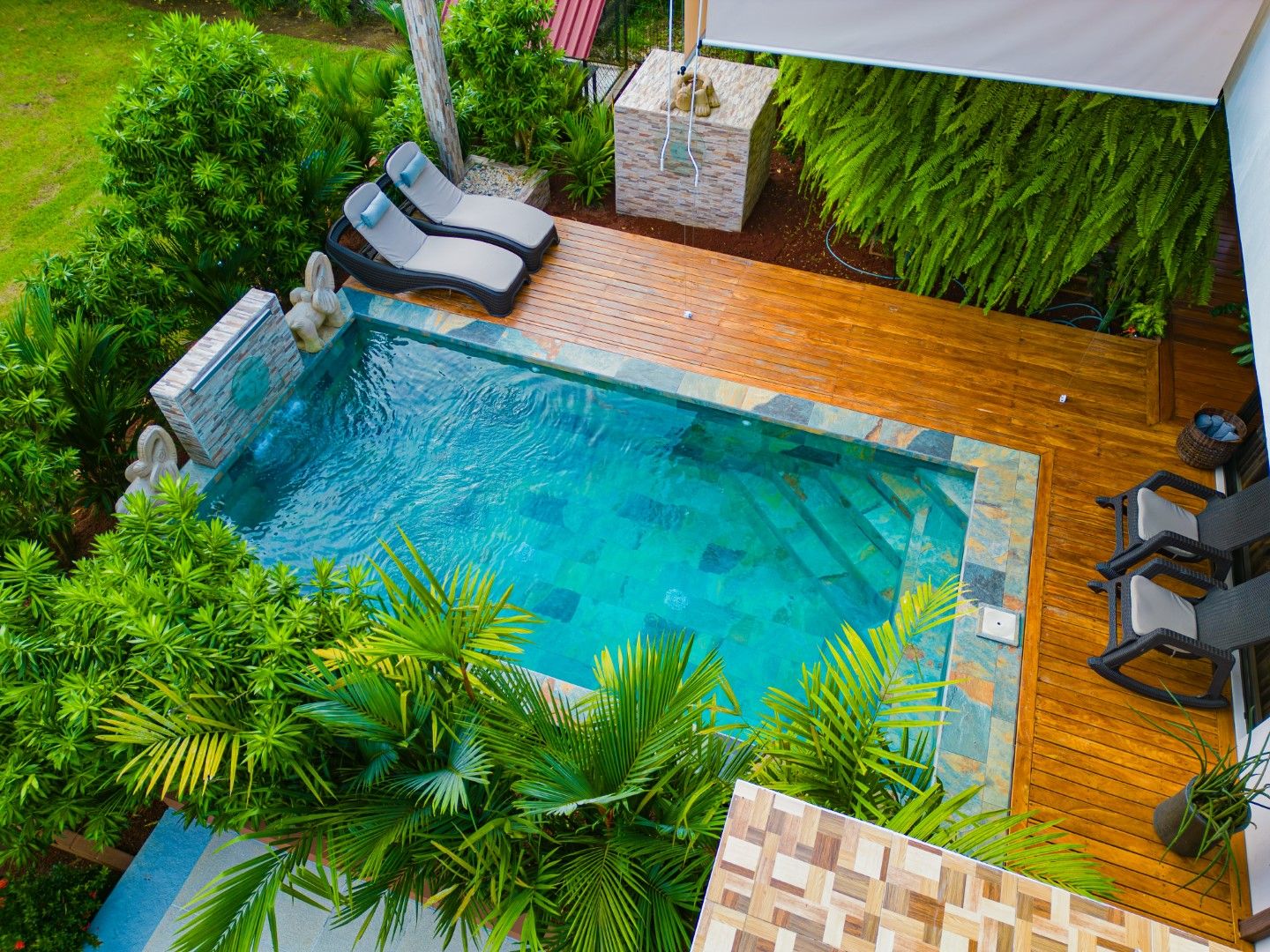 Luxury private pool with wooden deck and tropical landscaping viewed from above.