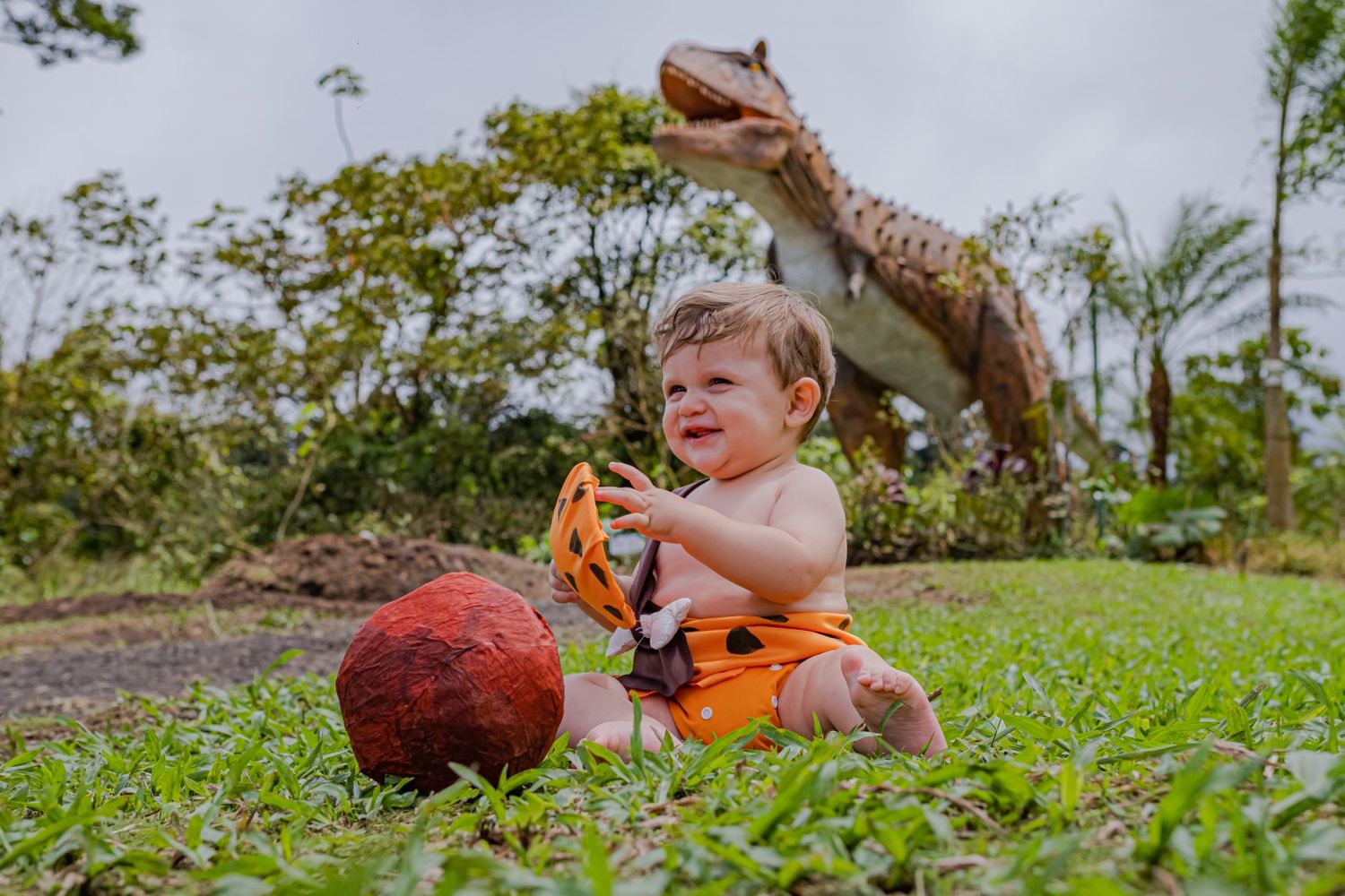 Young child playing with toy dinosaurs outdoors on grass.