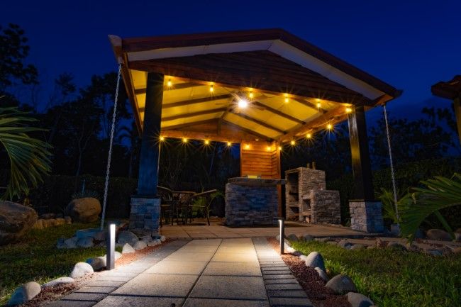 Outdoor terrace dining area illuminated at night with warm lighting and tropical garden surroundings.