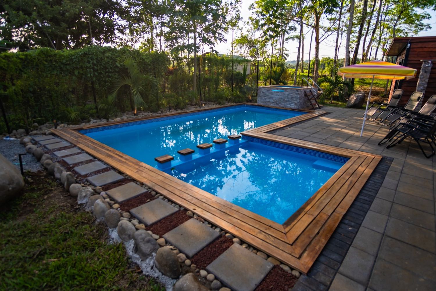 Swimming pool with wooden deck surround and natural stone landscaping in tropical setting.